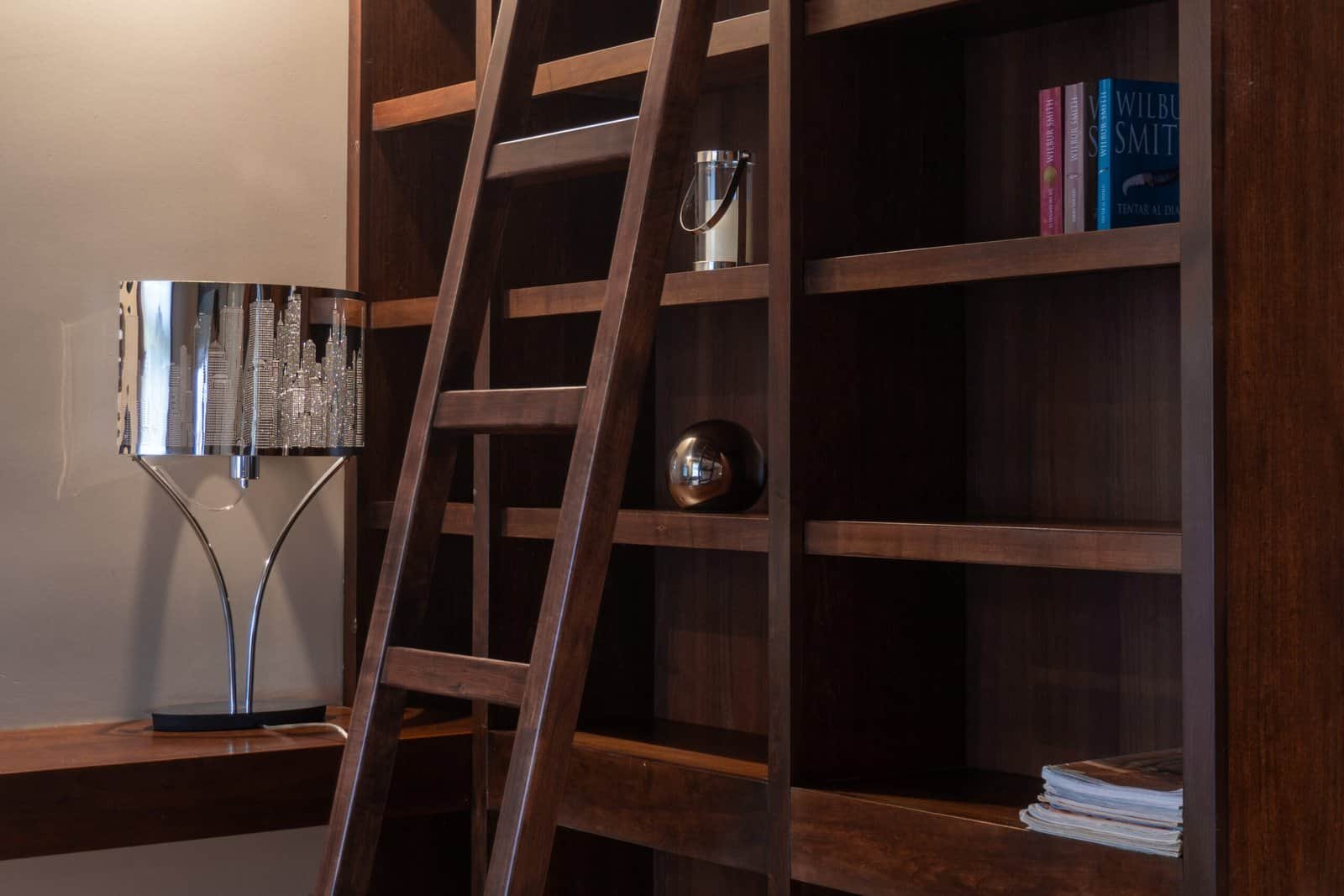 Wooden ladder leaning against a dark wood bookshelf with books and decor.
