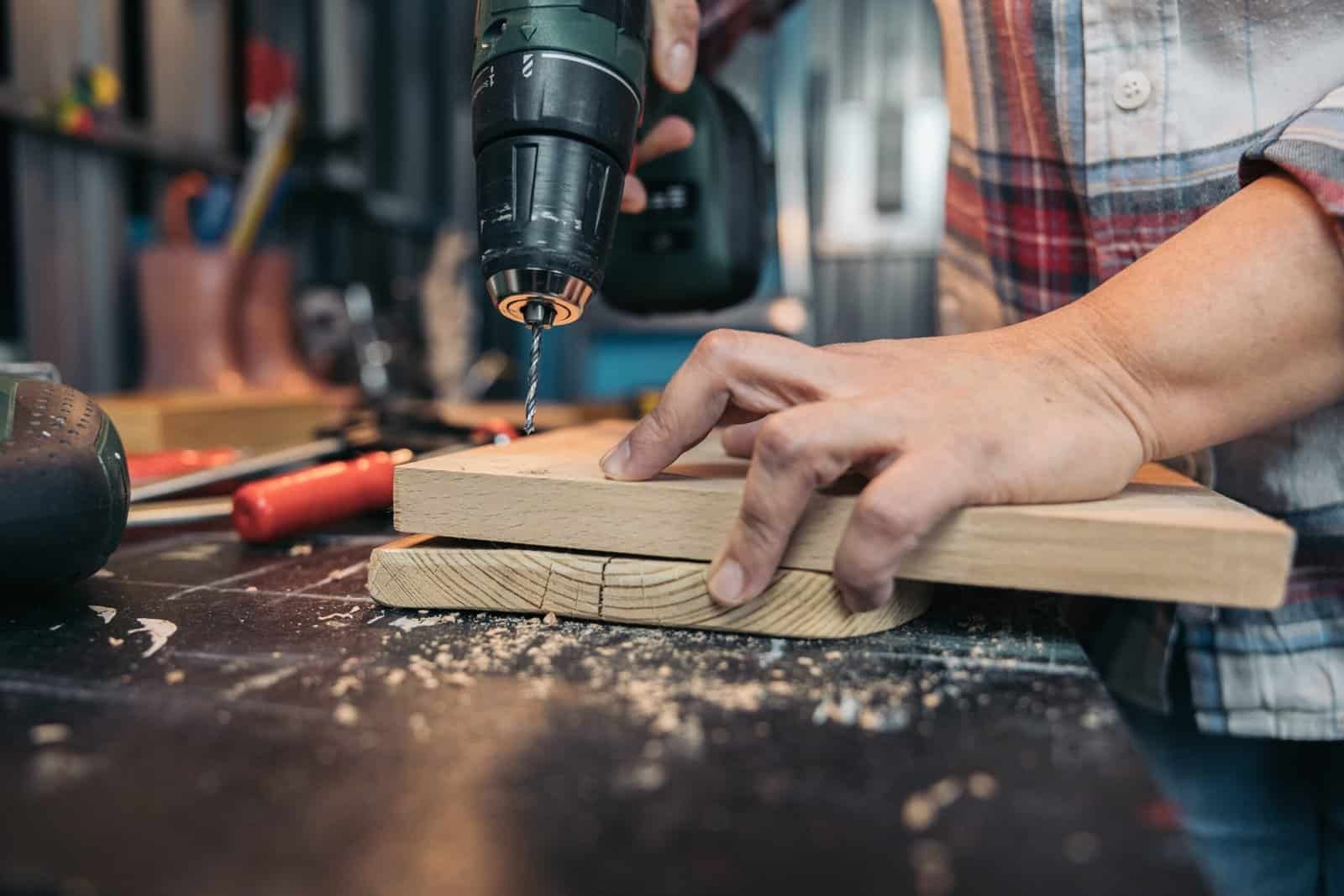 Person using a power drill on a wooden piece in a workshop.